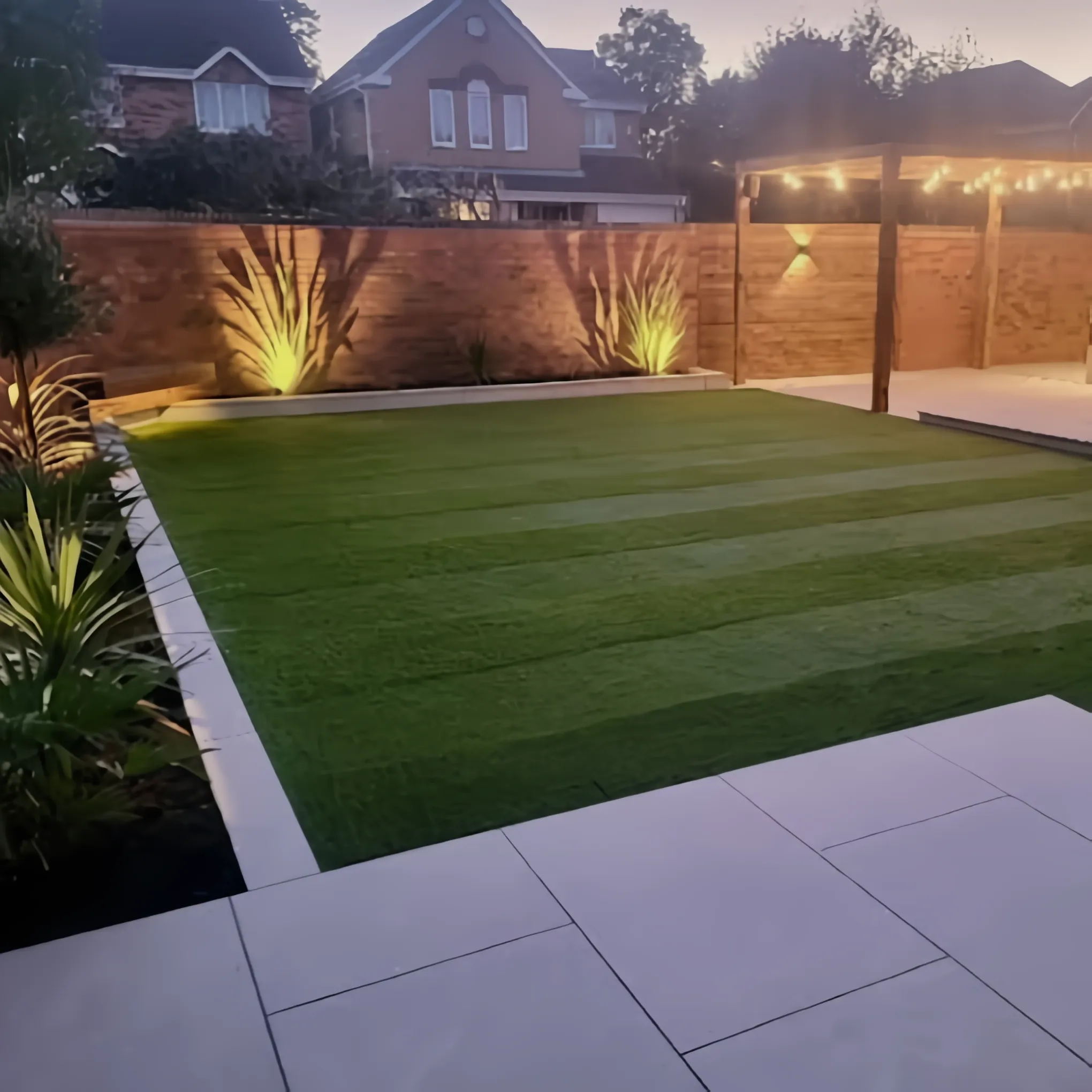Artificial lawn and porcelain patio lit with festoon lights at dusk